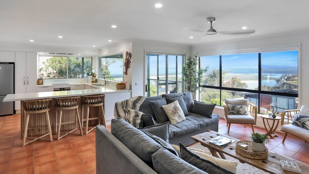 A modern living area with a large sofa, a dining table with bar stools, and a kitchen with a large island. - Rosies Seaview - 3 bedroom option (Merimbula)