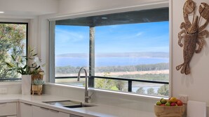 A modern kitchen with a large window, a sink, and a bowl of fruit on the counter. - Rosies Seaview - 3 bedroom option (Merimbula)