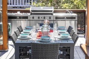 An outdoor dining area with a grill, wicker chairs, and a table set for six. - Sails to Sea - 4 bedroom pet friendly (Pambula Beach)