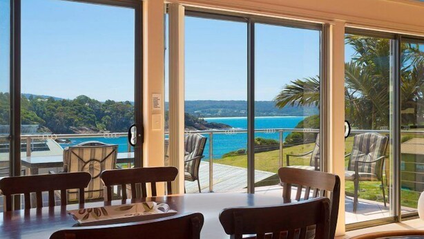 A dining area with a table and chairs, large windows with a view of a coastal landscape. - Snug Cove Villas located at Eden Wharf (Eden)
