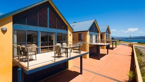A modern building with large windows and a balcony with outdoor seating. - Snug Cove Villas located at Eden Wharf (Eden)
