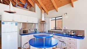 A modern kitchen with a blue island, white cabinets, and stainless steel appliances. - Snug Cove Villas located at Eden Wharf (Eden)