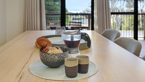 A dining table with a bowl of pastries, a coffee maker, and two cups.