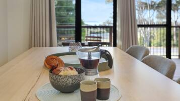A dining table with a bowl of pastries, a coffee maker, and two cups.