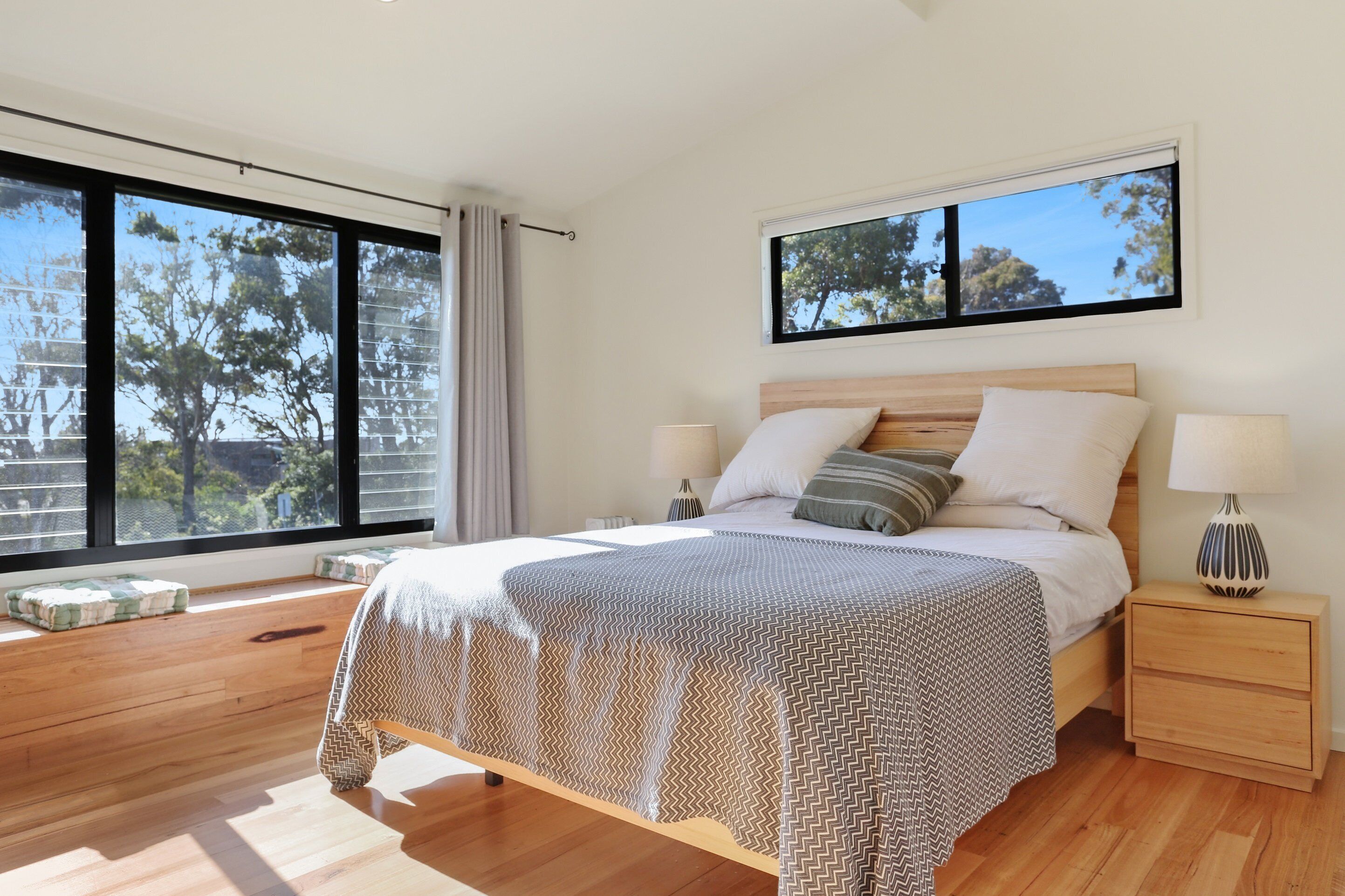A modern bedroom with a large bed, two bedside tables, and a window with a view of trees.