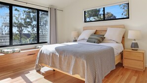 A modern bedroom with a large bed, two bedside tables, and a window with a view of trees.