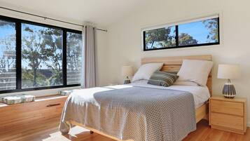 A modern bedroom with a large bed, two bedside tables, and a window with a view of trees.