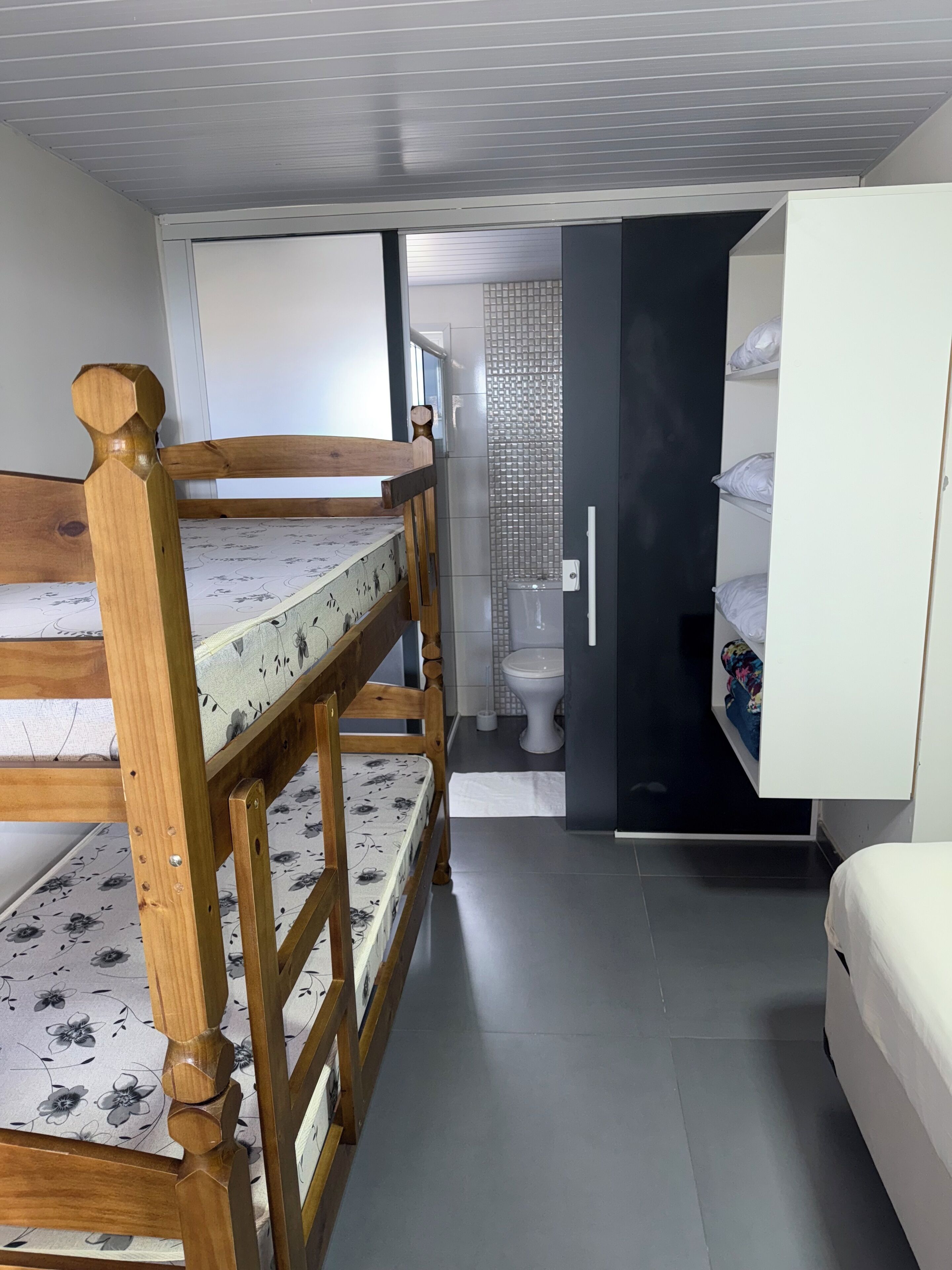 A compact room with a bunk bed, a small bathroom with a toilet and a shower, and a white wardrobe.