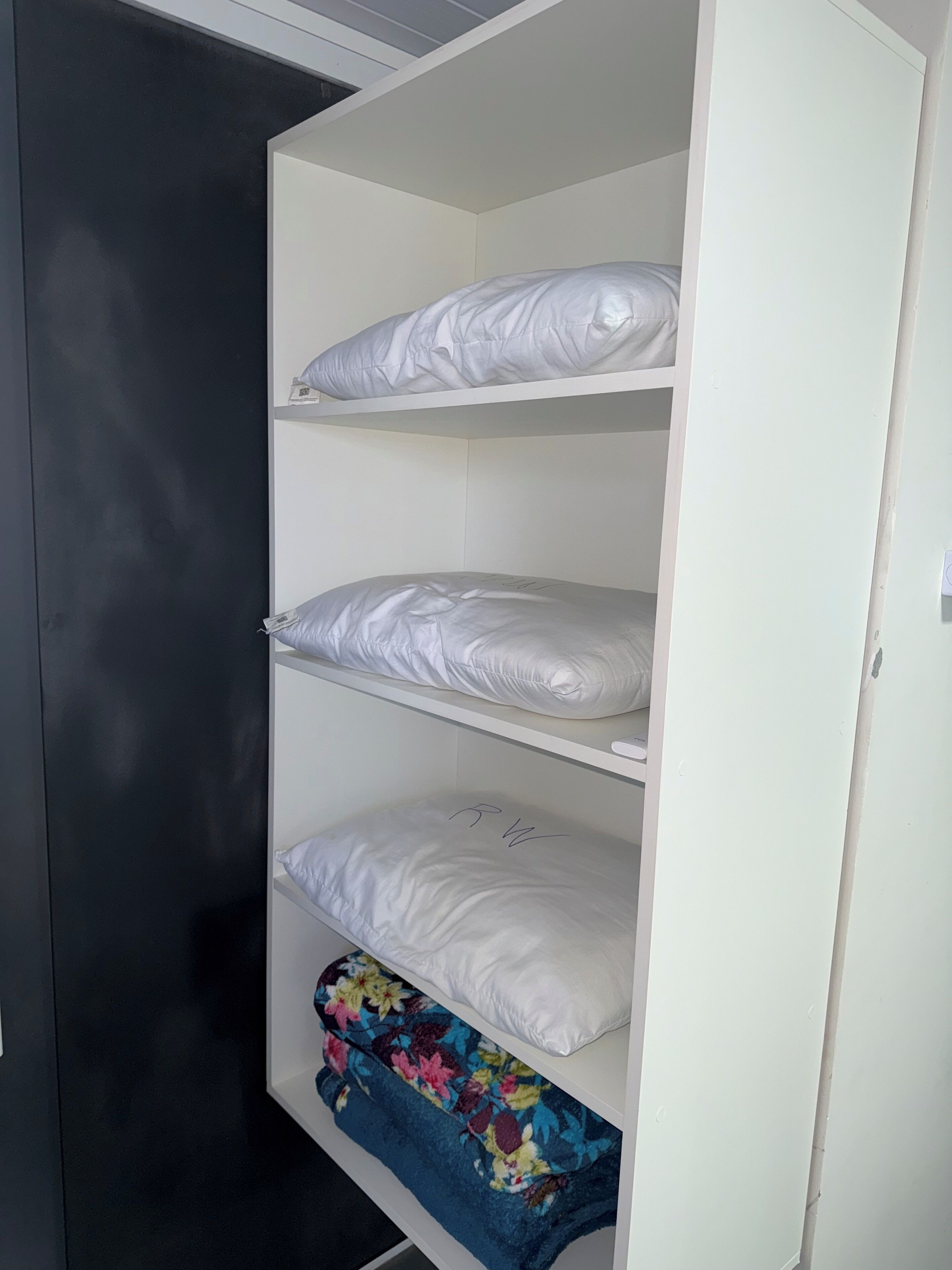 A bunk bed with white bedding and a floral blanket on the lower shelf.