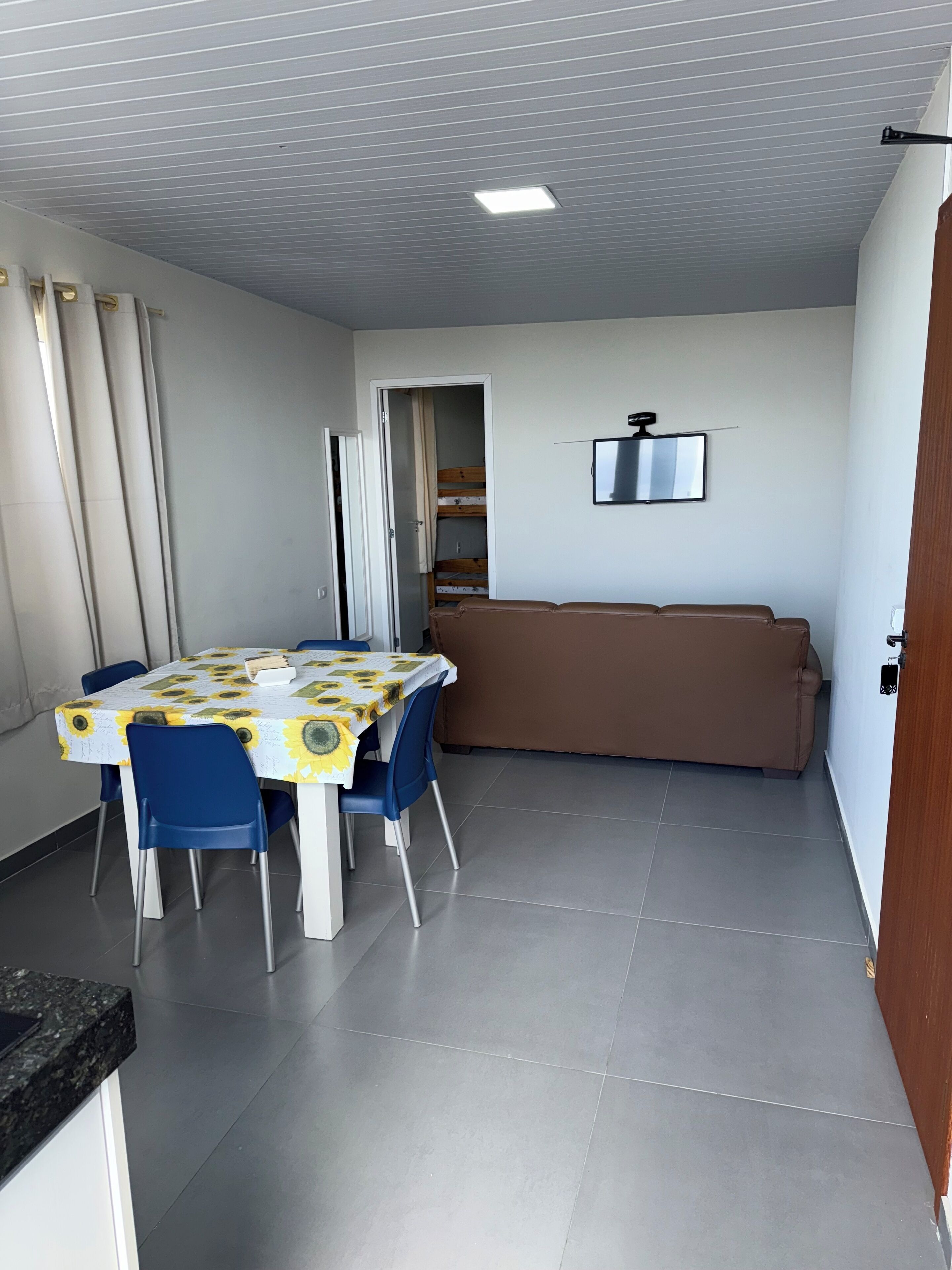 Un espacio habitable compacto con una mesa de comedor, sillas azules, un sofá marrón y un televisor montado en la pared.