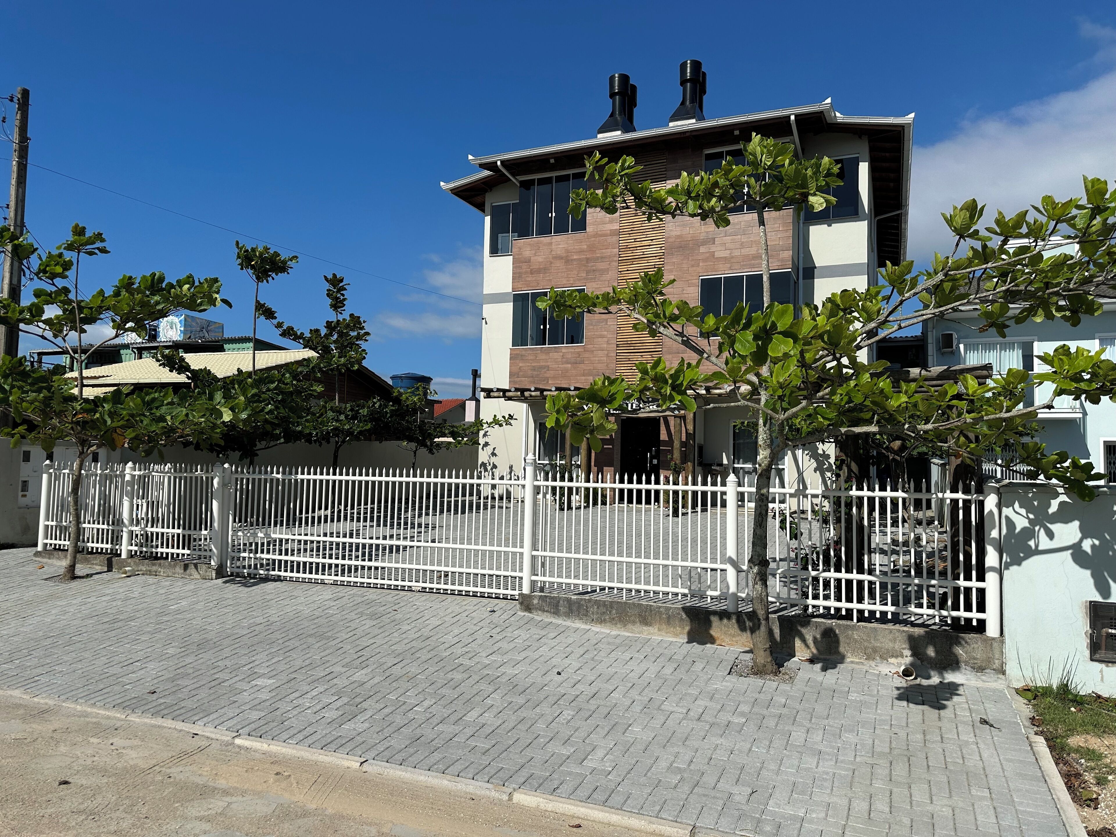 A modern two-story building with a white fence, paved walkway, and trees.