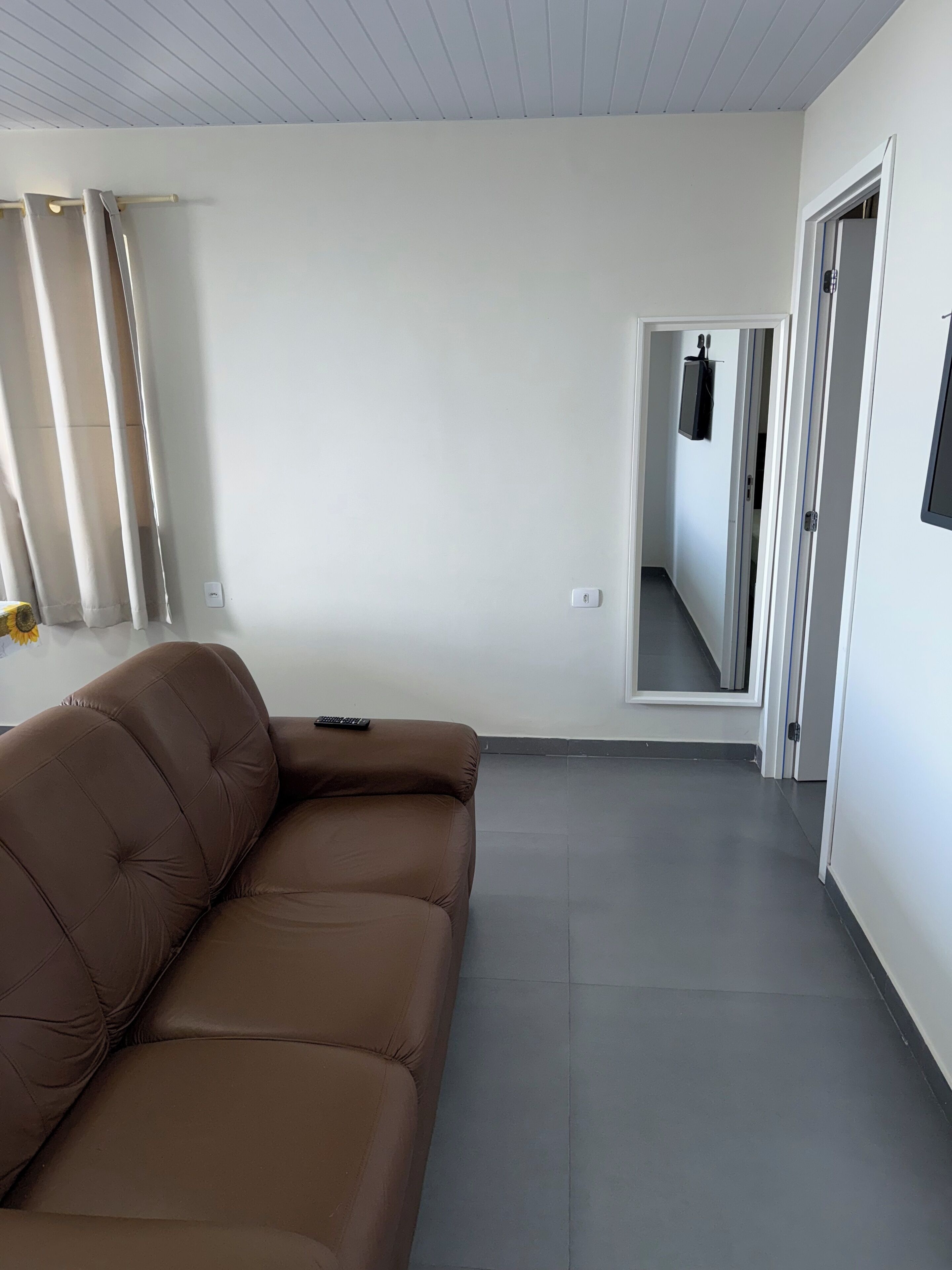 Una sala de estar moderna con un sofá de cuero marrón, un televisor de pantalla plana montado en la pared y un pasillo que conduce a otra habitación.