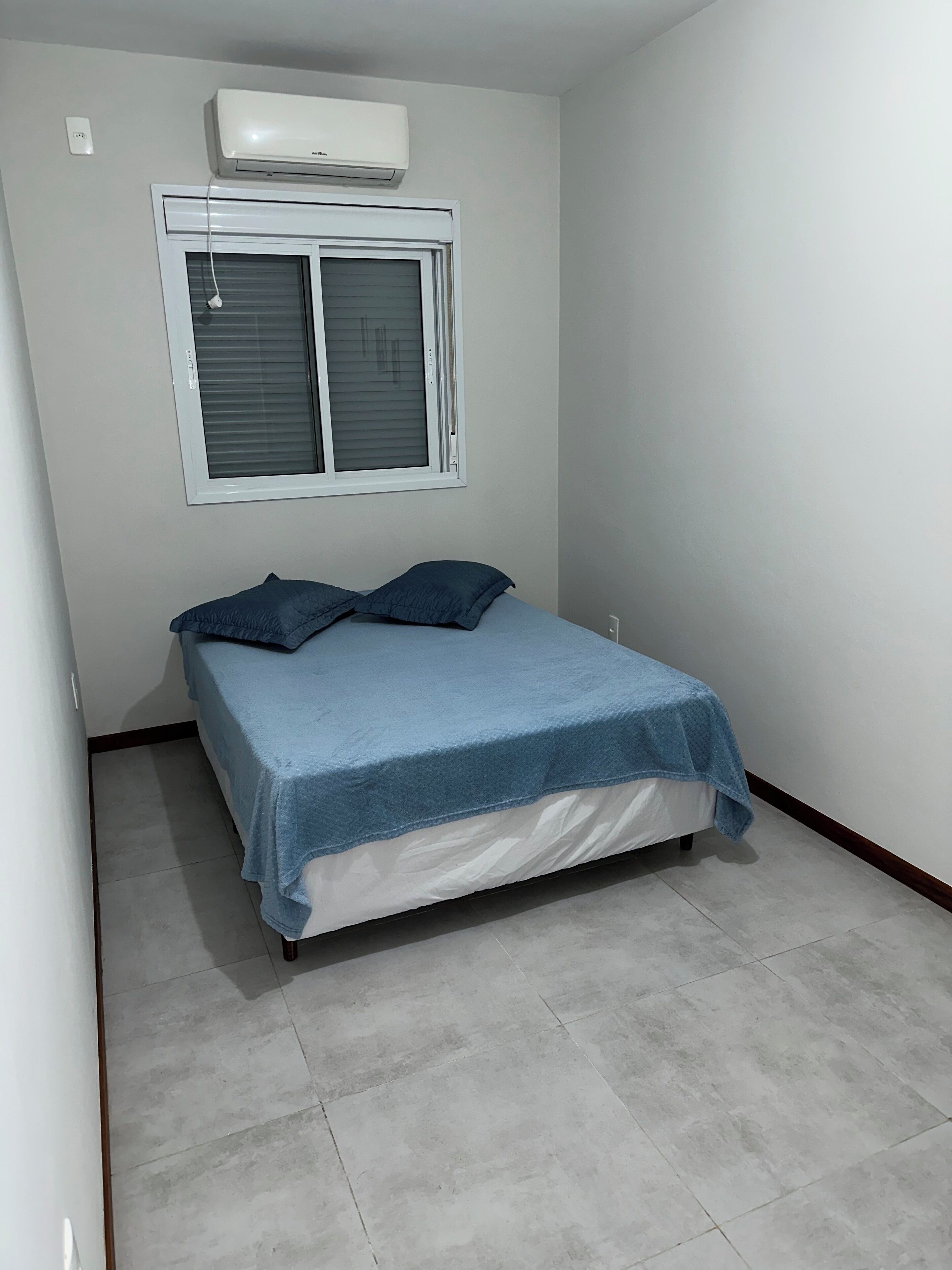 Een slaapkamer met een bed, een raam met zonwering en een airconditioner.