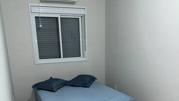 Een slaapkamer met een bed, een raam met zonwering en een airconditioner.