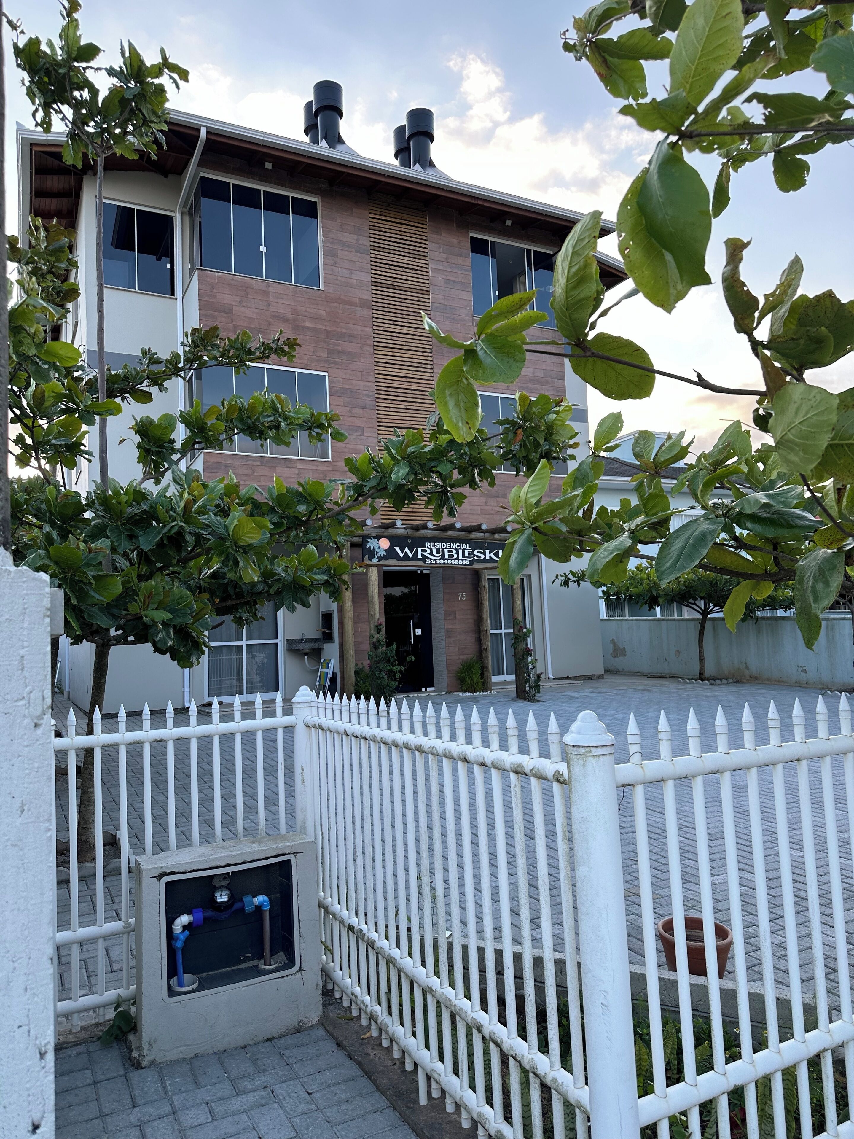 A residential building with a brick facade, large windows, and a white picket fence.