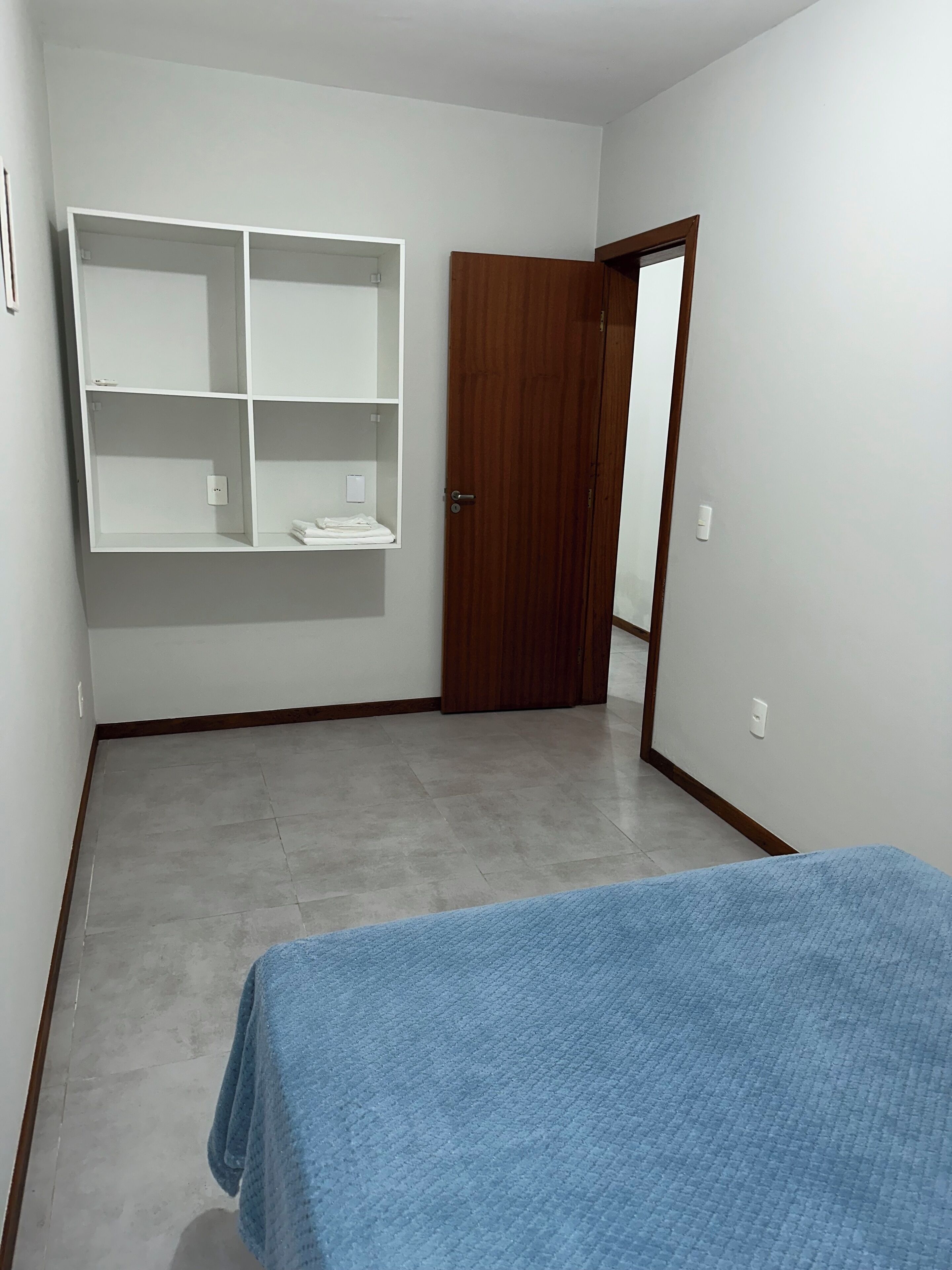A room with a bed, a wooden door, and a white shelving unit.