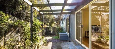 A covered patio with a pergola, a small garden area, and a sliding glass door leading to an interior space.