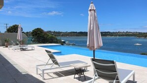 Un espace aménagé au bord de la piscine, avec des chaises longues et des parasols, donnant sur une étendue d’eau où se trouvent des bateaux.