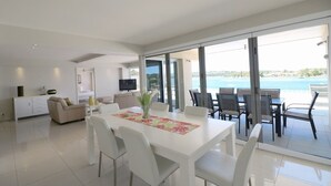 A modern living room with a dining area, large windows, and a view of the sea. - Sybella - 6 Bedroom Option incredible views and a pool (Merimbula)