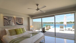 A bedroom with a large bed, a ceiling fan, and a view of the sea through large windows. - Sybella - 6 Bedroom Option incredible views and a pool (Merimbula)