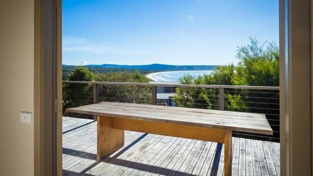 A wooden deck with a bench, overlooking a beach and mountains.