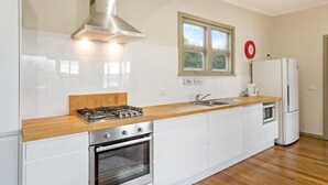 A modern kitchen with white cabinets, a wooden countertop, a stainless steel range hood, a built-in oven, a refrigerator, and a window with a view of greenery.