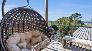 A hanging chair with a cushioned seat and back, a bench, and a view of the sea and trees. - Shore Break 5: Unlimited wifi and right at the beach (Eden)