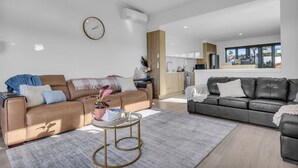A modern living room with two sofas, a coffee table, and a kitchen in the background. - Shore Break 5: Unlimited wifi and right at the beach (Eden)
