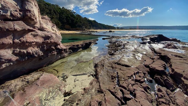 A rocky shoreline with clear water, a sandy beach, and a forested hill in the background. - Shore Break 5: Unlimited wifi and right at the beach (Eden)
