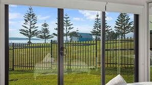 Una habitación con un gran ventanal corredera que da a un espacio exterior con césped y vistas a árboles y una masa de agua.