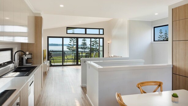 Una cocina moderna con vistas a un lago, una zona de comedor con mesa y sillas, y un gran ventanal corredero que da a un espacio exterior.
