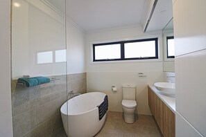 A modern bathroom with a freestanding bathtub, a toilet, and a sink. - Shore break 6: Right at the beach (Eden)