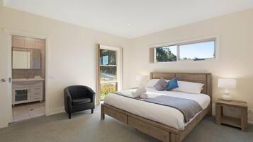 A bedroom with a bed, bedside tables, a chair, a window, and a bathroom with a sink and mirror.