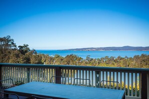 Une terrasse avec une table et des chaises, offrant une vue sur la côte, avec des arbres et des collines.