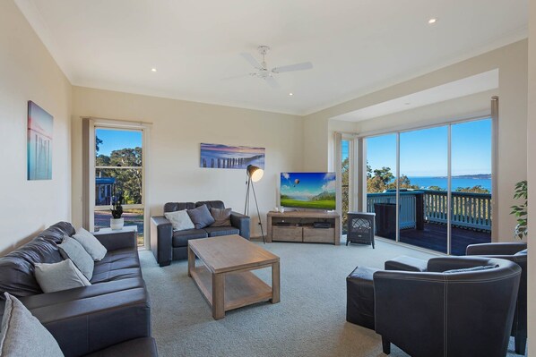 A spacious living room with a large window, a ceiling fan, and a view of the sea.
