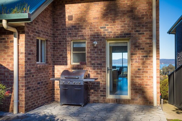 Une maison en briques avec un barbecue, deux fenêtres et une vue sur la mer.