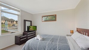 Un dormitorio con cama, cómoda, televisor y un cuadro en la pared.