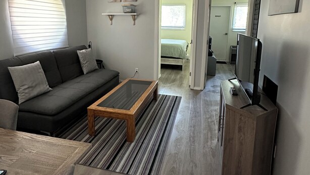 Un salon moderne avec un canapé, une table basse et un meuble pour la télévision. Un couloir mène à une autre pièce.