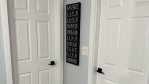 Un couloir avec deux portes blanches, un mur de couleur gris clair et un panneau affichant une citation inspirante.