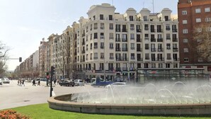Un edificio de varios pisos con balcones y una fuente al frente.