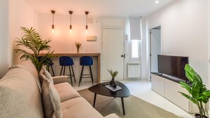 Una sala de estar moderna con un sofá, una mesa de centro, un televisor y un comedor con sillas y una mesa pequeña.