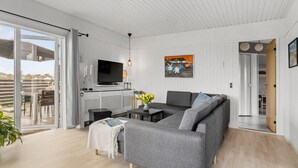 Ein modernes Wohnzimmer mit einem grauen Sofa, einem Flachbildfernseher, einem Couchtisch und einem großen Fenster.