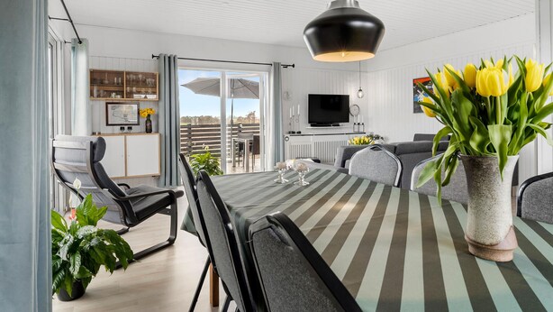 Ein modernes Wohnzimmer mit einem gestreiften Tisch, einem grauen Sofa und einem großen Fenster mit Vorhängen.