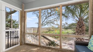 A covered porch with a view of a landscaped area including a palm tree and a wooden deck. - Savor the morning light from the decks and porches; close to lighthouse and ferry (Bald Head Island)