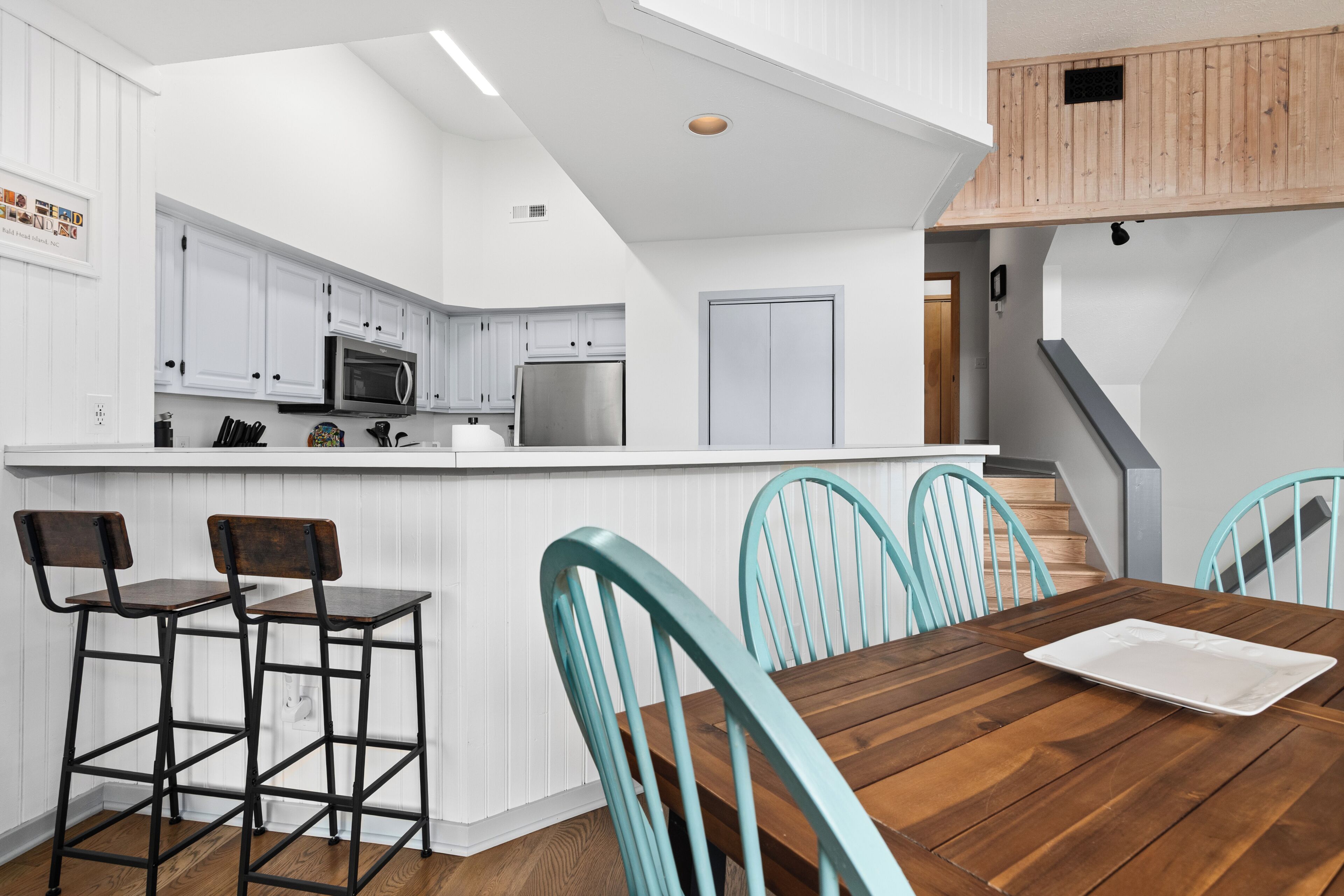 A modern kitchen with white cabinetry, a wooden dining table, and teal chairs.