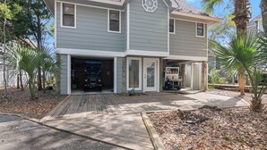 A two-story house with a garage, a covered porch, and a small garden with palm trees. - Savor the morning light from the decks and porches; close to lighthouse and ferry (Bald Head Island)
