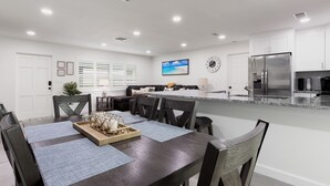 A modern kitchen with white cabinets, a stainless steel refrigerator, and a dining area with a dark wooden table and chairs.
