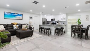 A modern kitchen with a central island, bar stools, and a dining area with a table and chairs.