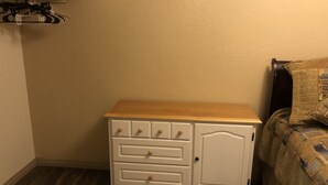 Een kleine, witte ladekast met een houten blad en lades, geplaatst naast een bed met een gestreept deken.
