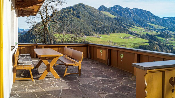 Un patio con pavimento in pietra, mobili in legno e vista su un paesaggio montuoso.